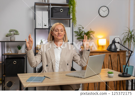 Caucasian calm mature businesswoman in suit meditating after using laptop at home office desk 125372175