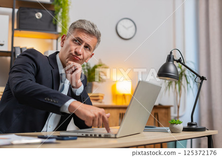 Young businessman using laptop while thinking about important creative project decision at desk 125372176