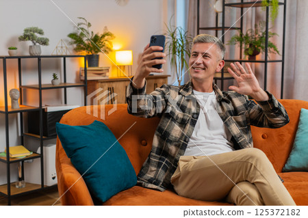 Happy young man taking selfie on smartphone communicating video call home online with subscribers Happy young man taking selfie on smartphone communicating video call home online with subscribers 125372182