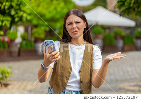 Upset young woman using smartphone typing browsing, loses becoming shocked bad news on city street Upset young woman using smartphone typing browsing, loses becoming shocked bad news on city street 125372197