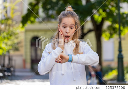 Young woman worrying to be punctual, with anxiety checking time on watch, running late to transport 125372208
