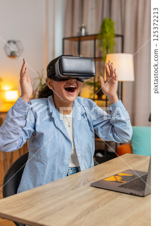 Surprised young Indian woman freelancer using VR headset while sitting at home office table desk 125372213