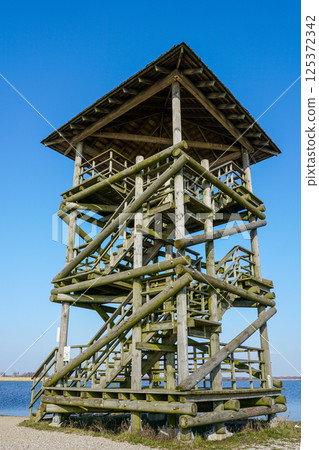 Bird and nature observation tower made of round wooden logs against the blue sky 125372342