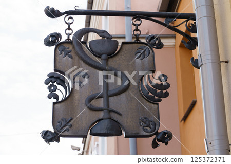 Elegant metal pharmacy sign featuring a serpent and cup design 125372371