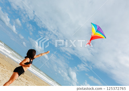 low angle view of small girl flying a kite on the beach 125372765