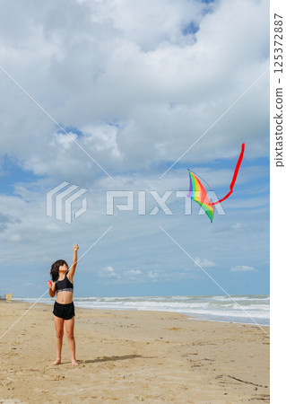 wide angle view of small girl flying a kite on the beach 125372887