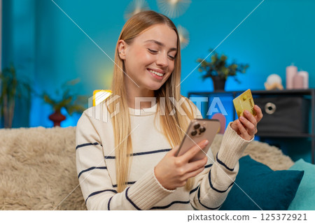 Caucasian woman paying purchase on sofa with mobile phone credit card smiling successful indoors 125372921