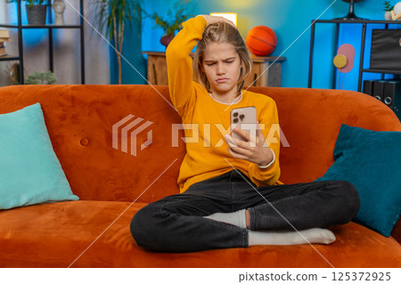 Teenager boy upset losing online game on smartphone, despair, sitting on sofa, indoors at home Teenager boy upset losing online game on smartphone, despair, sitting on sofa, indoors at home 125372925
