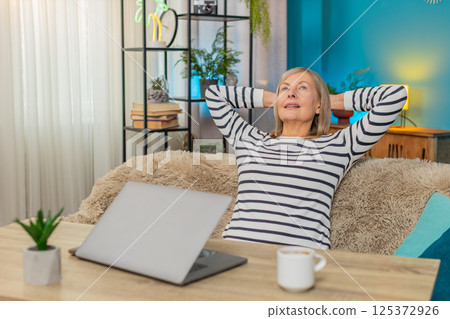 Mature woman happily closing laptop after completing important task, smiling and relaxing at table Mature woman happily closing laptop after completing important task, smiling and relaxing at table 125372926