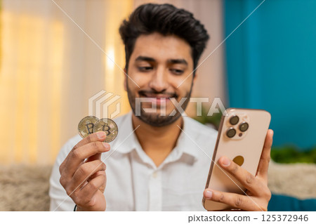 Indian man checking bitcoin wallet balance on smartphone, excited and slightly tense about market 125372946