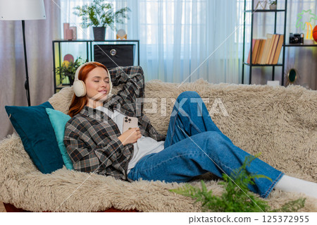 Woman lying on sofa with eyes closed listening to audiobook imagining scenes with peaceful emotion Woman lying on sofa with eyes closed listening to audiobook imagining scenes with peaceful emotion 125372955