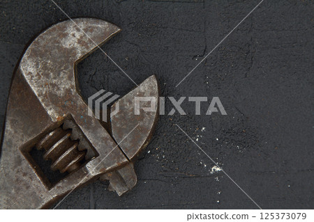 Old adjustable wrench on rusty metal sheet. Sliding forged wrench against a dark background 125373079