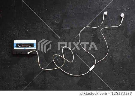 Blue -White audio cassette and cassette pleer with headphones on a black background. 125373187