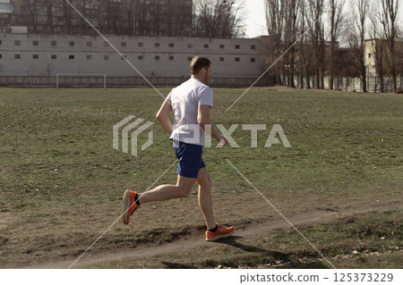 A professional runner dressed in a white T-shirt and blue sports shorts is running in the summer in the city 125373229