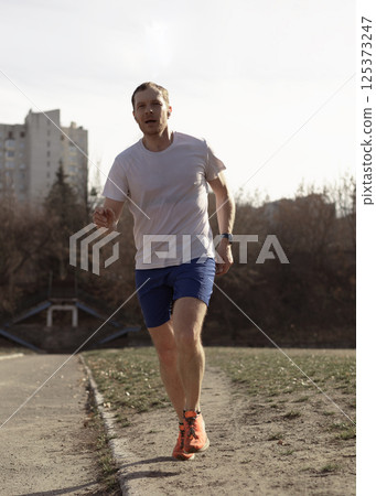 Male professional runner doing sports outdoors on a soccer field outside the city 125373247