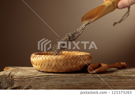 Chia seeds are poured into a wicker bowl. 125373263