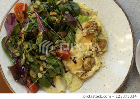 omelet with lettuce, cherry tomatoes and pumpkin seeds on white plate 125373334