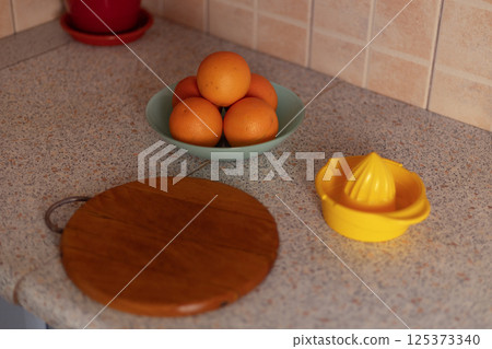 On the table are a plate of oranges, a cutting board, and a citrus juicer 125373340
