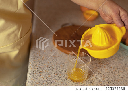 Close-up of a mature woman's hands pouring freshly squeezed orange juice into a glass 125373386