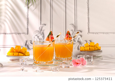 Summer party concept and Detox diet, Modern still life with tropical fruits. Homemade cocktail, juice or lemonade with mango slices and ice on sunny kitchen table. Restaurant menu Summer party concept and Detox diet, Modern still life with tropical fruits. Homemade cocktail, juice or lemonade with mango slices and ice on sunny kitchen table. Restaurant menu 125373411