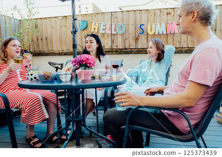 Friends enjoying summer gathering on private outdoor patio terrace with drinks and snacks. Friends dining, drinking cocktails, having fun together on patio party event. Millennials lifestyle concept 125373439