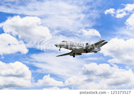 Private business plane flying under a blue sky with white clouds 125373527