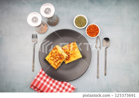 Slices of baked Round Borek cheese pie in kitchen tray with herbs. Dark background. Top view. Copy space Slices of baked Round Borek cheese pie in kitchen tray with herbs. Dark background. Top view. Copy space 125373691