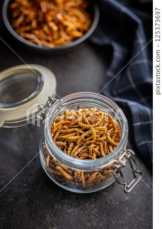 Dried salted worms. Roasted mealworms in jar on black table. 125373697