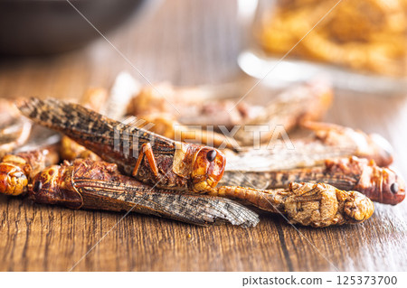 Dried salted insect. Roasted grasshoppers on wooden table. 125373700