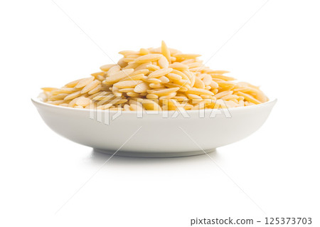 Orzo, kritharaki, risoni pasta. Uncooked dry pasta in bowl isolated on white background. Orzo, kritharaki, risoni pasta. Uncooked dry pasta in bowl isolated on white background. 125373703