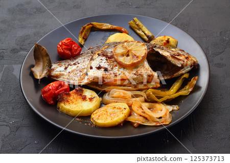 Delicious grilled dorado or sea bream fish with salad, spices, grilled dorada on a black plate. Delicious grilled dorado or sea bream fish with salad, spices, grilled dorada on a black plate. 125373713