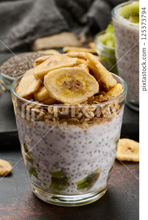Glass of chia seed pudding layered with kiwi, topped with granola and banana chips Glass of chia seed pudding layered with kiwi, topped with granola and banana chips 125373794