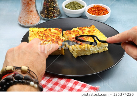 Slices of baked Round Borek cheese pie in kitchen tray with herbs. Dark background. Top view. Copy space Slices of baked Round Borek cheese pie in kitchen tray with herbs. Dark background. Top view. Copy space 125374226