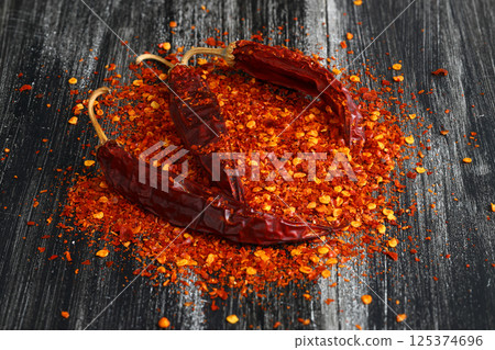 Wooden bowl with crushed chili pepper and fresh red chili pepper on old table. Selective focus. Wooden bowl with crushed chili pepper and fresh red chili pepper on old table. Selective focus. 125374696