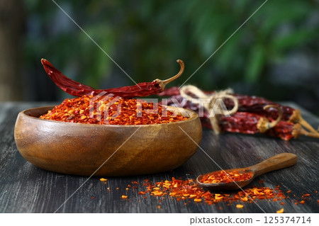 Wooden bowl with crushed chili pepper and fresh red chili pepper on old table. Selective focus. Wooden bowl with crushed chili pepper and fresh red chili pepper on old table. Selective focus. 125374714