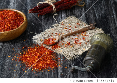 Wooden bowl with crushed chili pepper and fresh red chili pepper on old table. Selective focus. Wooden bowl with crushed chili pepper and fresh red chili pepper on old table. Selective focus. 125374715