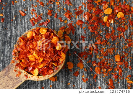 Wooden bowl with crushed chili pepper and fresh red chili pepper on old table. Selective focus. 125374716