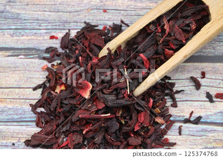 Karkade tea. Hibiscus tea leaves in wooden scoop isolated on wooden background. File contains clipping path. Top view. Karkade tea. Hibiscus tea leaves in wooden scoop isolated on wooden background. File contains clipping path. Top view. 125374768