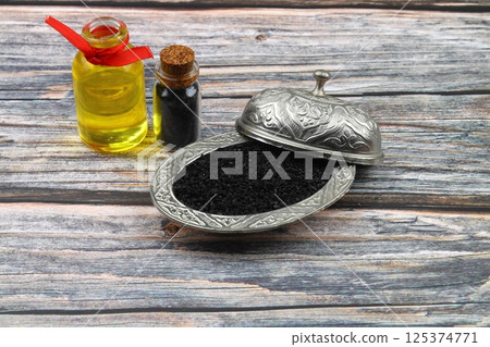 Black cumin seeds and essential oil with bowl and wooden shovel or spoon. Nigella Sativa in glass bottle. Organic herbal medicine for many diseases 125374771