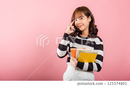 Portrait of beautiful Asian young woman teenage smiling hugging books, female person holding book and thinking idea, studio shot isolated on pink background with copy space, education concept 125374801
