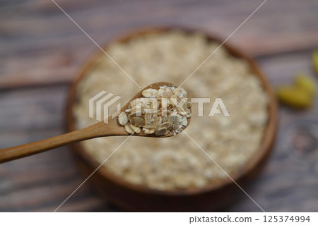 Breakfast cereals in wooden spoon. Healthy muesli with oat flakes, nuts and raisins isolated on wooden background. Selective Focus. 125374994