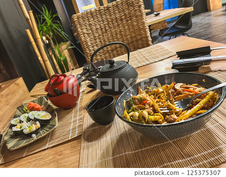 Spaghetti with chicken, mushrooms and sesame seeds on a plate in a asian food restaurant with teapot and chopsticks 125375307