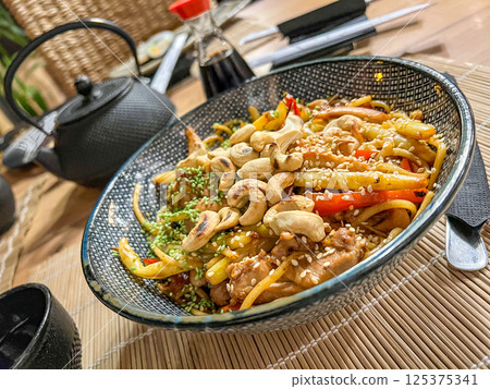 Spaghetti with chicken, mushrooms and sesame seeds on a plate in a asian food restaurant with teapot and chopsticks 125375341