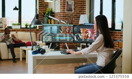 Freelancer asian woman video creator works on a movie project, multitasking with dual monitors, editing software and a color wheel in her home workspace. Film editing industry. Camera A. Freelancer asian woman video creator works on a movie project, multitasking with dual monitors, editing software and a color wheel in her home workspace. Film editing industry. Camera A. 125375559