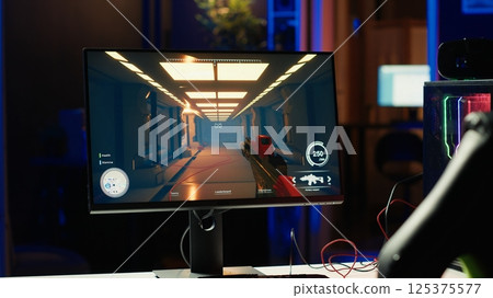 Shooting videogame on PC with neon lights illuminated components in empty apartment. Science fiction game on desktop PC monitor next to virtual reality glasses and computer peripherals 125375577