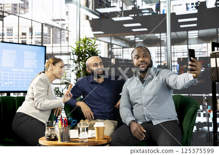 Man and colleagues talking selfie picture after successful briefing meeting to share ideas for profit growth. Employees in office talking photos with smartphone after working on startup evolution Man and colleagues talking selfie picture after successful briefing meeting to share ideas for profit growth. Employees in office talking photos with smartphone after working on startup evolution 125375599