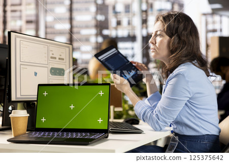 Woman employee examines business data next to mockup display, working hard at the office to meet deadlines and achieve objectives. Young adult studies infographics on computer. Woman employee examines business data next to mockup display, working hard at the office to meet deadlines and achieve objectives. Young adult studies infographics on computer. 125375642