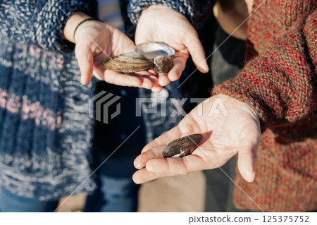 Seashells in hands, close-up. Young carefree couple in love throwing pebbles, shells, stones into sea outdoors. Fun family game together. High quality photo 125375752