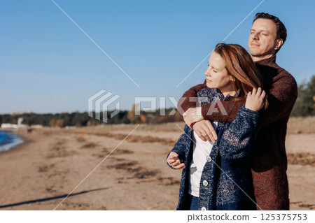 Loving couple walks on beach along sea on sunny autumn day. Weekend and lifestyle concept. High quality photo 125375753