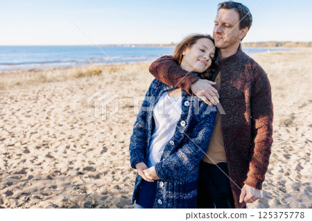 Loving couple walks on beach along sea on sunny autumn day. Weekend and lifestyle concept. High quality photo 125375778